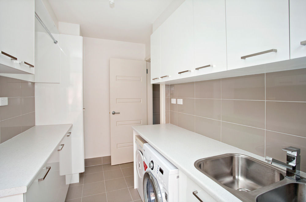 White laundry with beige wall tiles, a front-loader under the bench and a stainless sink